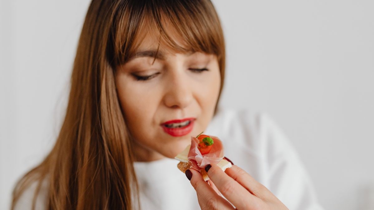Woman with long hair savoring a gourmet canape indoors.