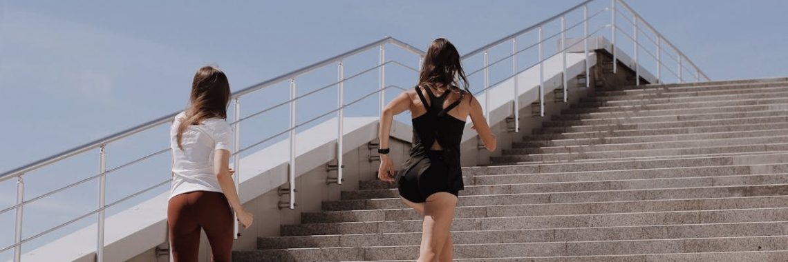 Two women running up stairs outdoors, embodying fitness and wellness.